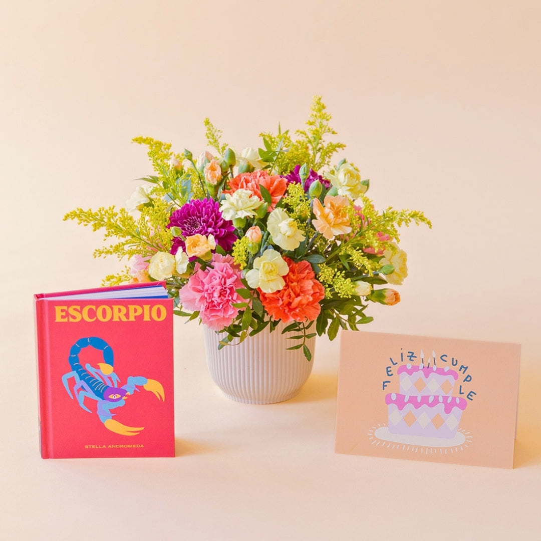 La Chispa - Arreglo floral con claveles, crisantemos y solidago junto a libro Escorpio y tarjeta de Colvin.