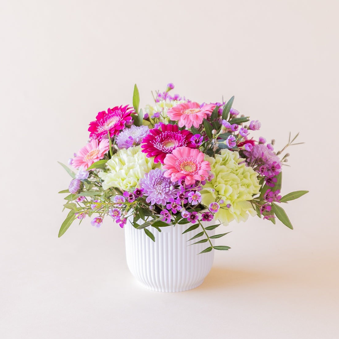 Arreglo floral mini Colvin con gerberas fucsia, claveles verdes y flores silvestres lilas en maceta estriada