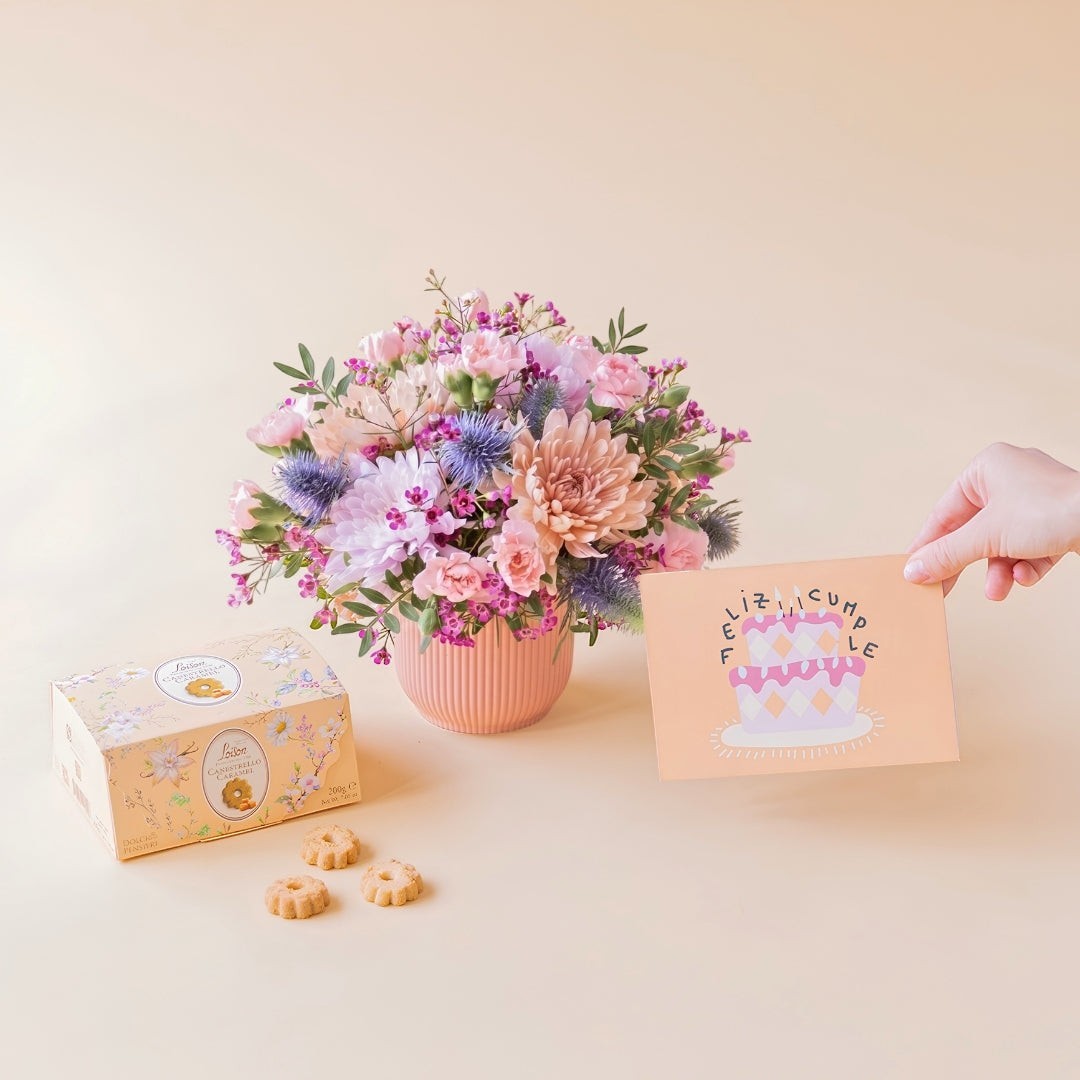 Arreglo floral Colvin con crisantemos malva, claveles rosas y cardos azules, junto a galletas Loison y tarjeta de cumple