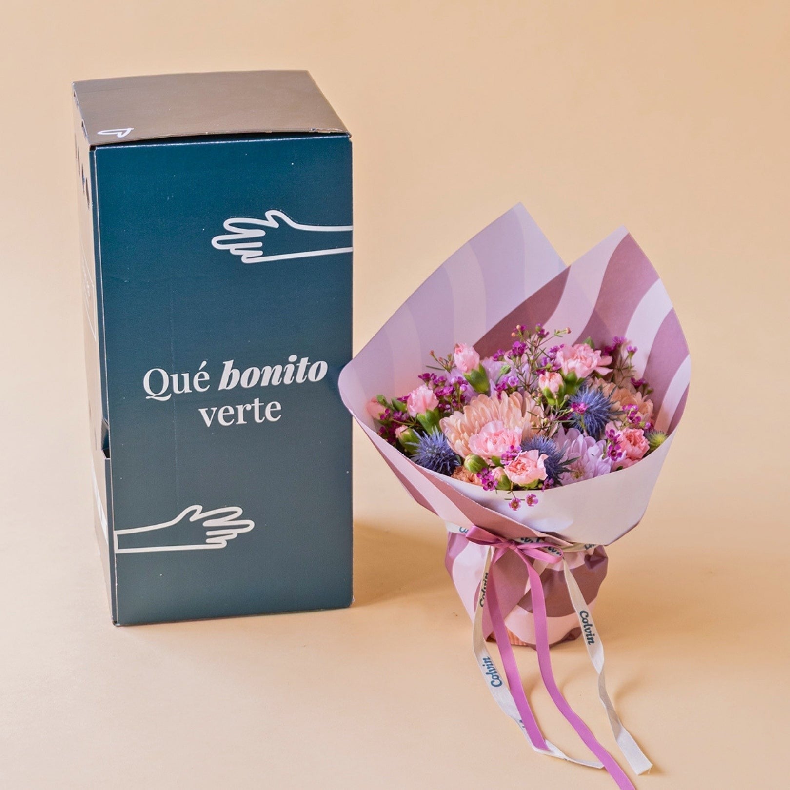 Arreglo floral Colvin con crisantemos malva, claveles rosas y cardos azules junto a una caja de regalo de cumpleaños.