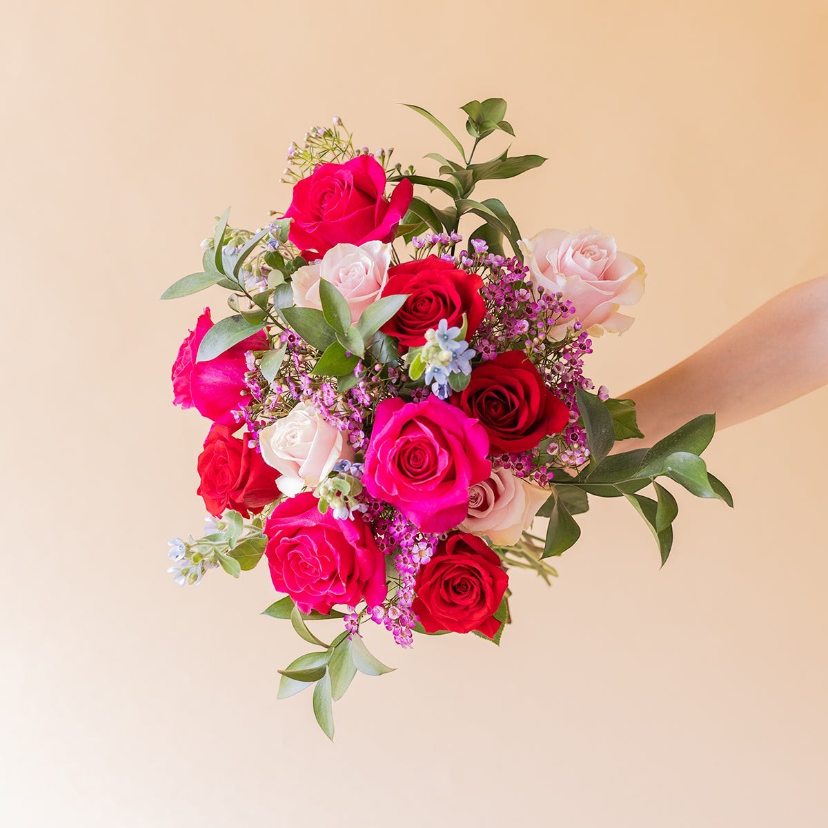 Ramo de rosas de colores variados con follaje verde de Colvin envuelto en papel kraft crema
