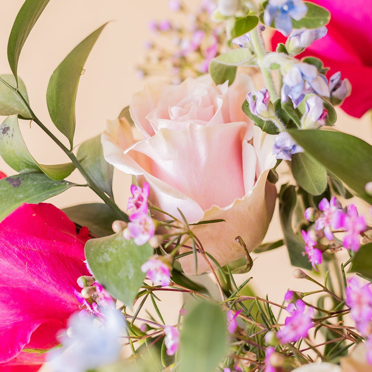Ramo de rosas de colores variados con flores silvestres y follaje verde de Colvin, presentado con estilo fresco.