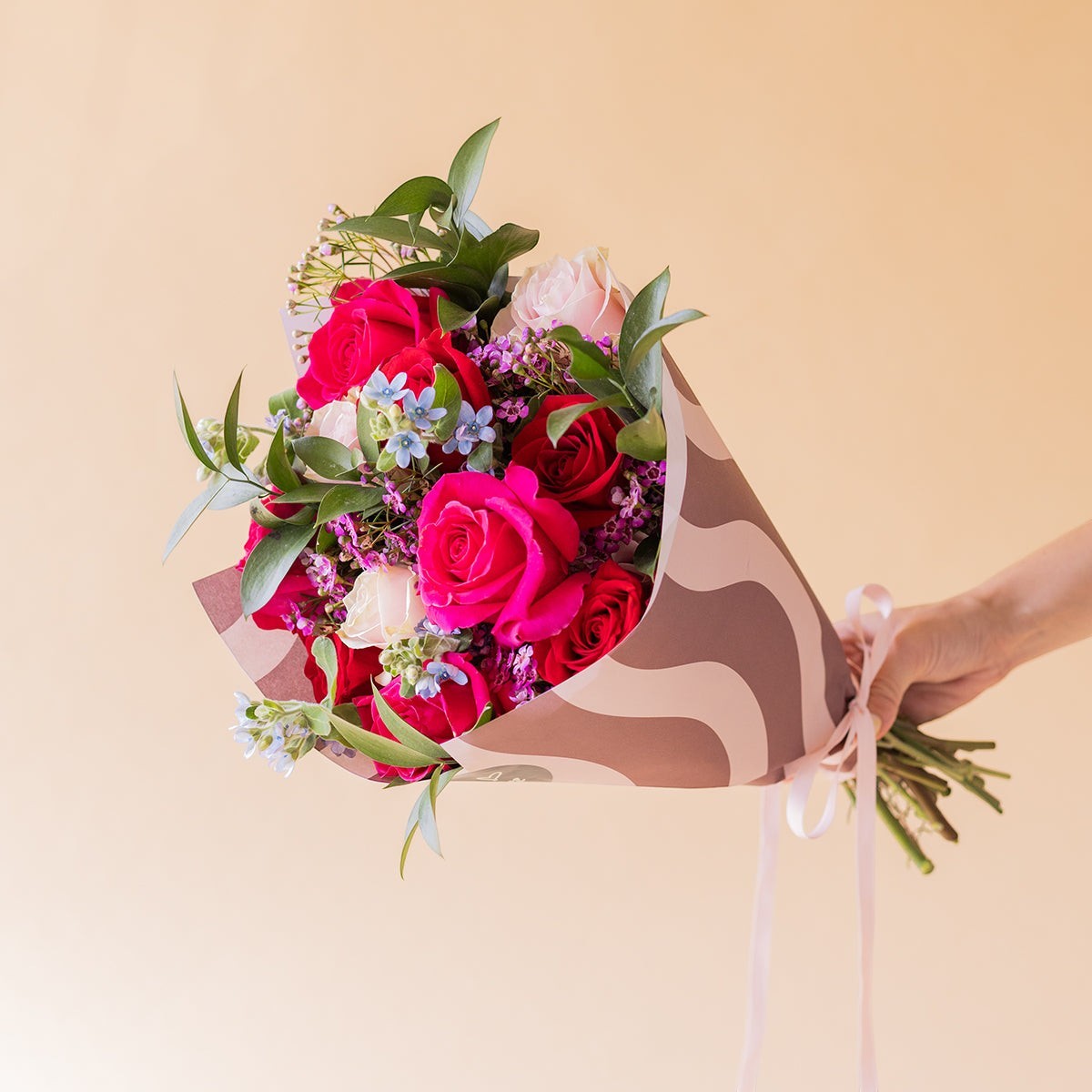 Ramo de flores Colvin El Encanto con rosas fucsias y rojas, envuelto en papel de diseño con ondas y lazo de raso.