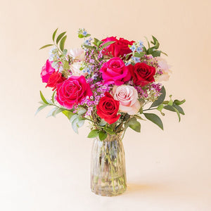 Ramo de rosas multicolores El Encanto de Colvin con flores variadas y follaje verde en un jarrón de cristal