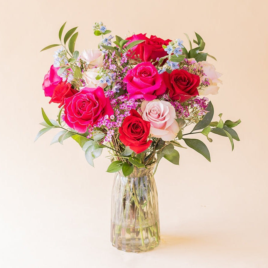 Ramo de rosas multicolores El Encanto de Colvin con flores variadas y follaje verde en un jarrón de cristal