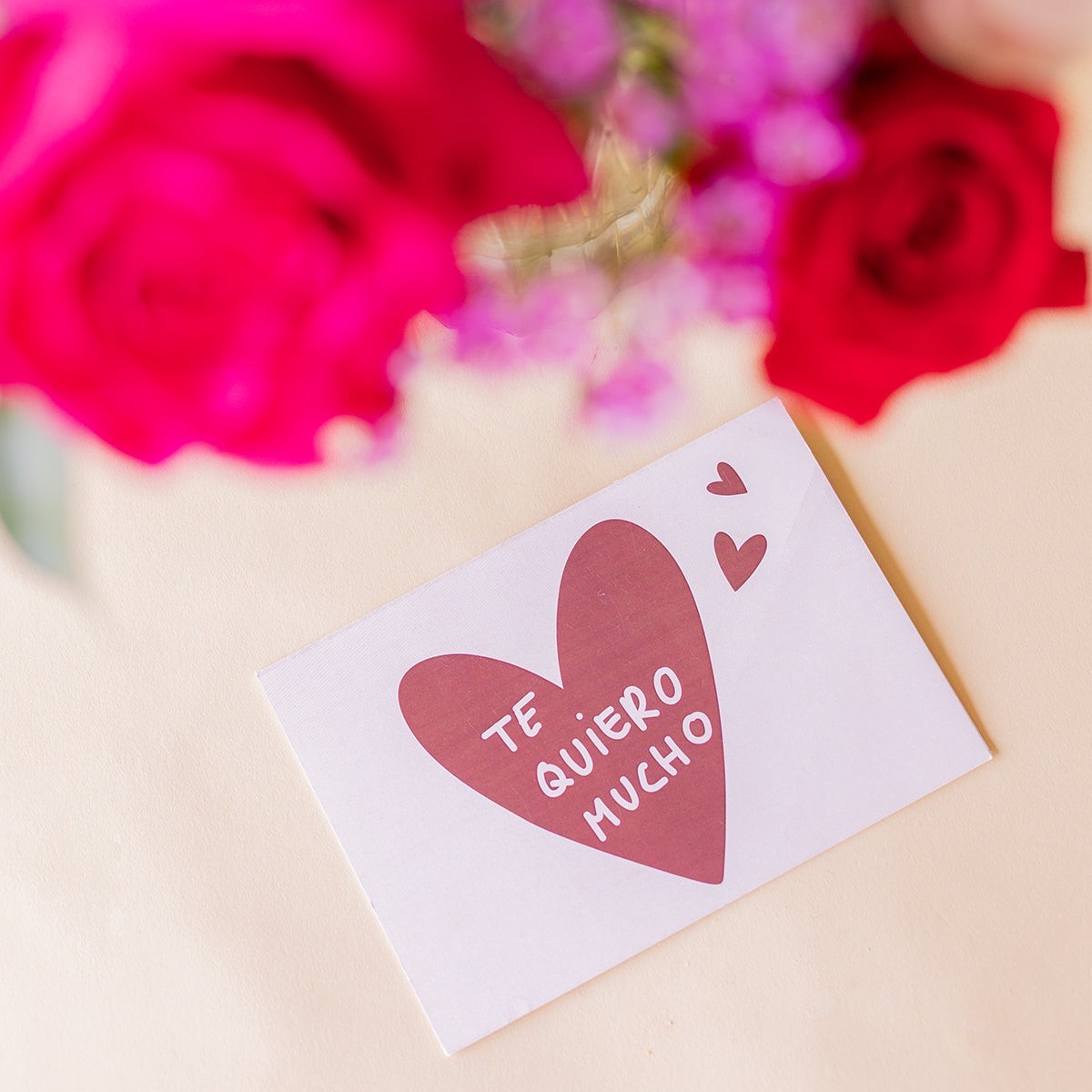 Tarjeta de regalo Colvin con mensaje Te quiero mucho y ramo de rosas fucsia y rojas de fondo