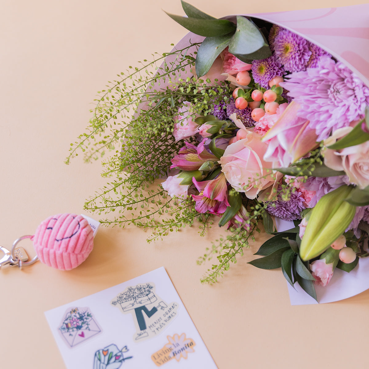 Ramo de flores pastel de Colvin con lirios rosas, crisantemos lilas, alstroemerias y hipericum, junto a llavero smiley rosa y stickers