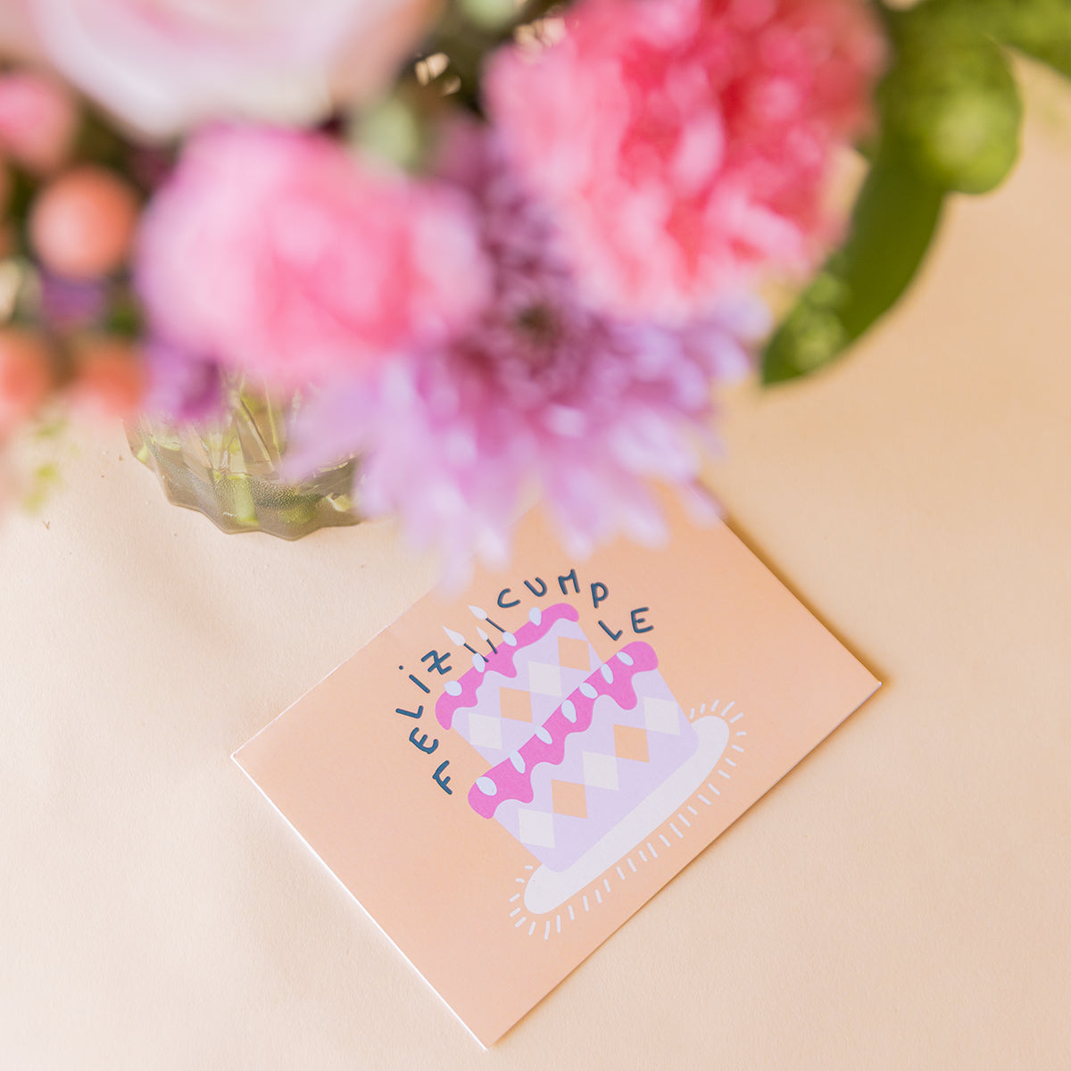 Tarjeta ilustrada "Feliz Cumple" con tarta de cumpleaños en tonos rosas, incluida en el ramo de flores de Colvin