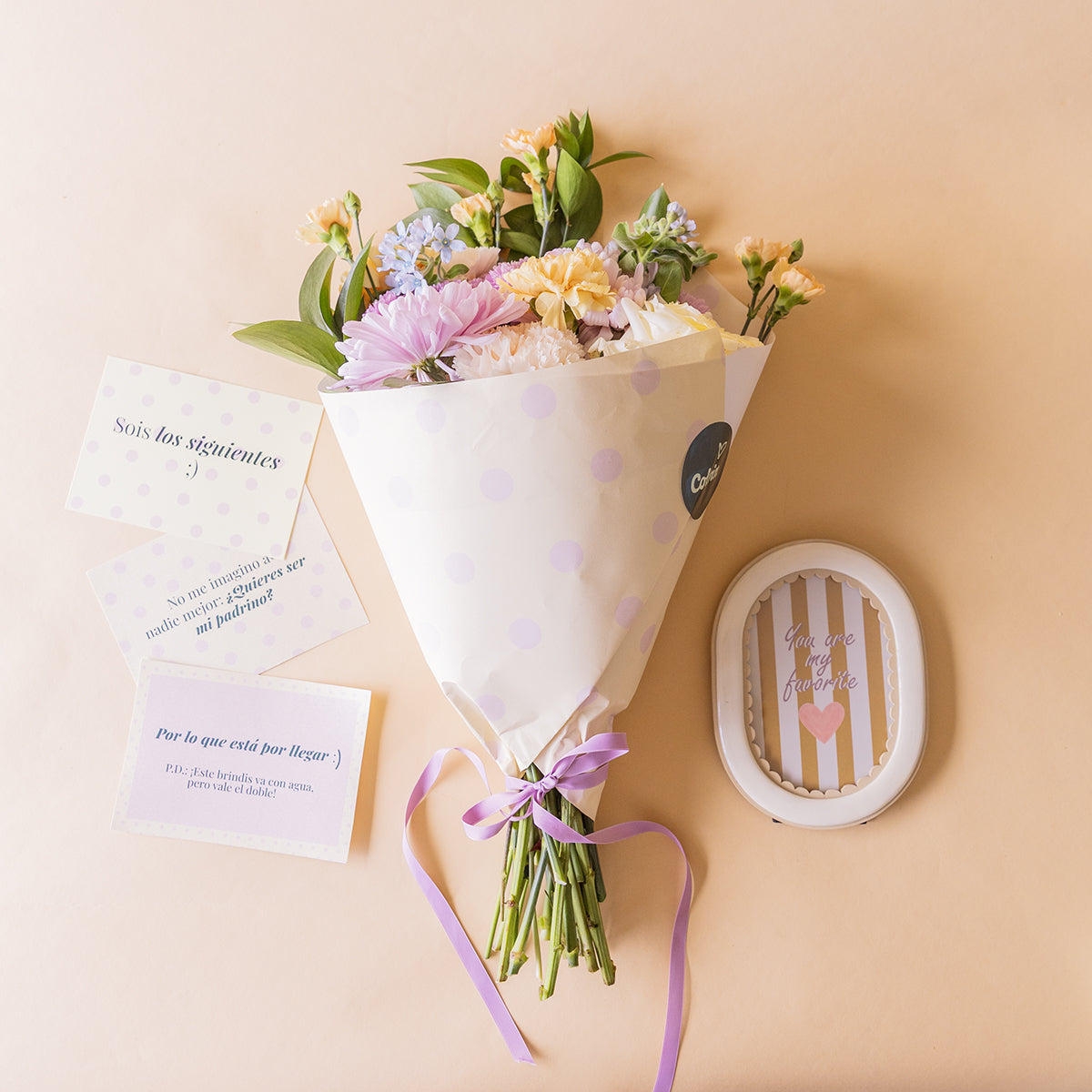 Ramo de flores pastel de Colvin con lazo lila junto a tarjetas de pedida de madrina y marco "You are my favorite"
