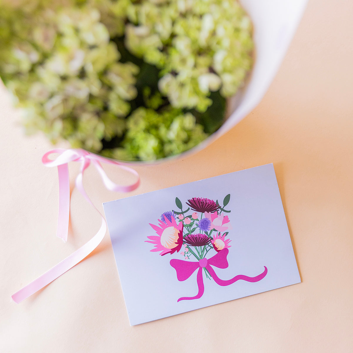 Cenital tarjeta protea floral junto a hortensia verde en envoltorio lunares con lazo rosa, planta regalo a domicilio - Colvin