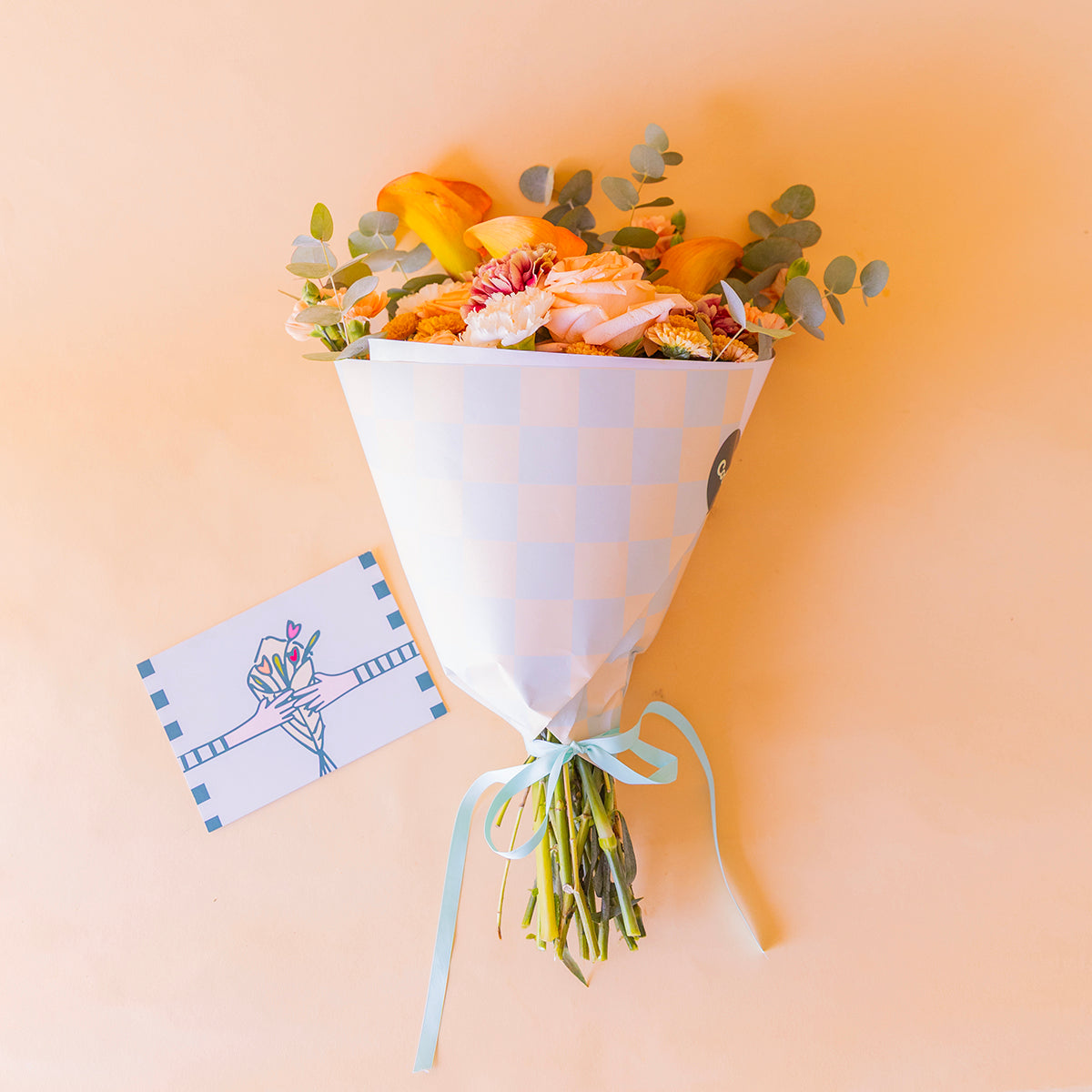 ramo Ginger en envoltorio cuadros blanco y azul con lazo celeste y tarjeta Más que Flores, vista cenital