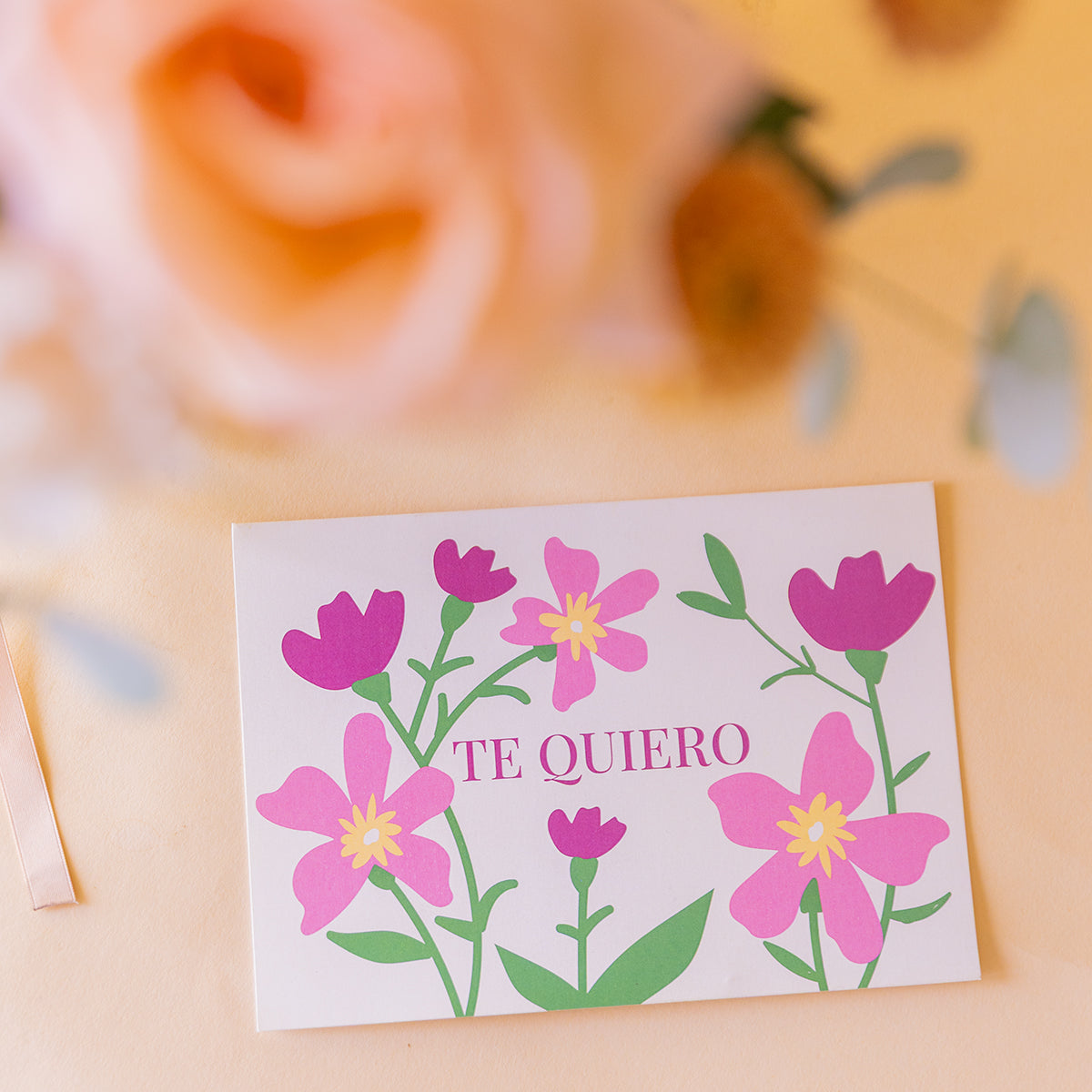 detalle macro de la tarjeta Te Quiero con ilustración floral rosa, ramo desenfocado al fondo