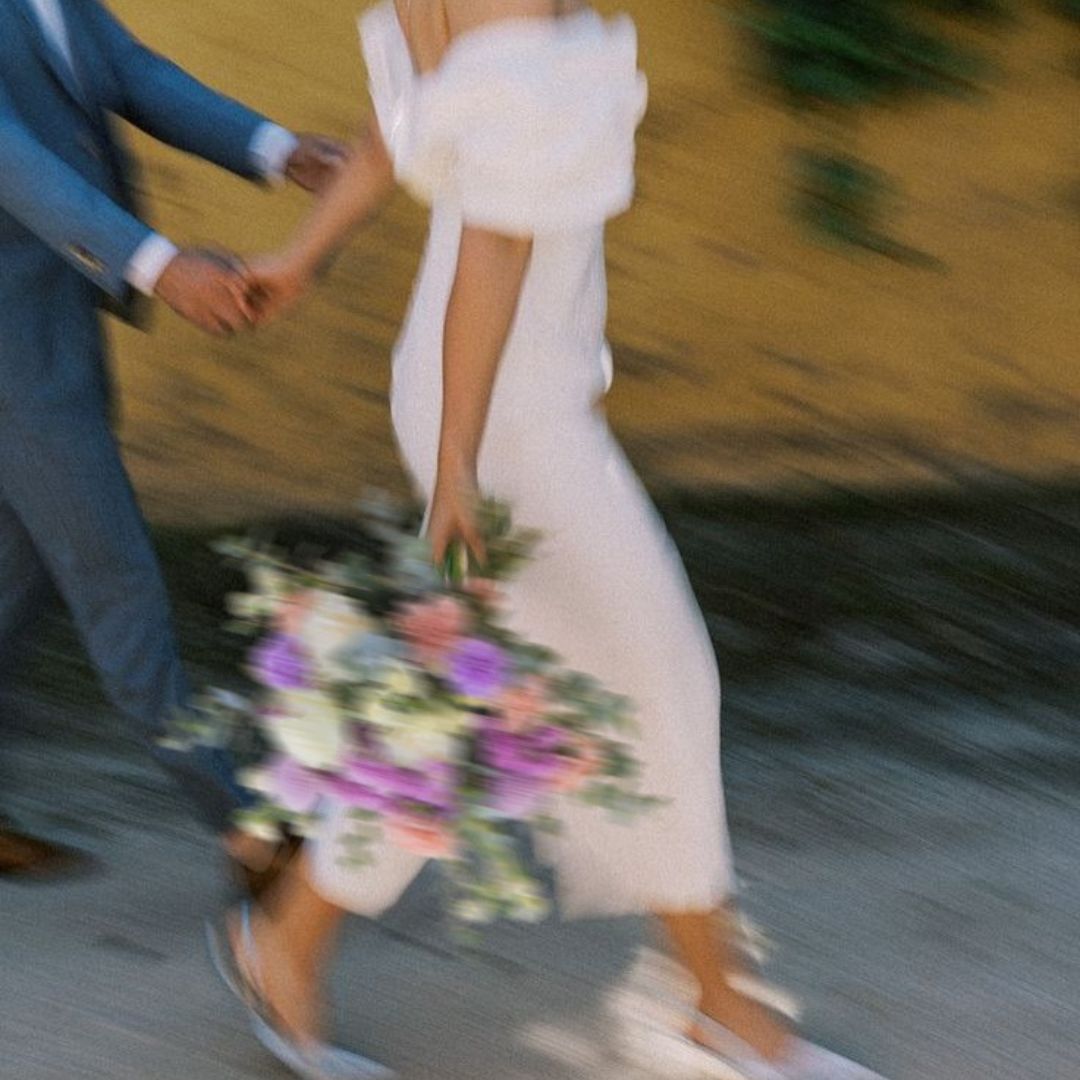 Novia con ramo de flores en tonos lilas, blancos y rosas caminando de la mano el día de su boda