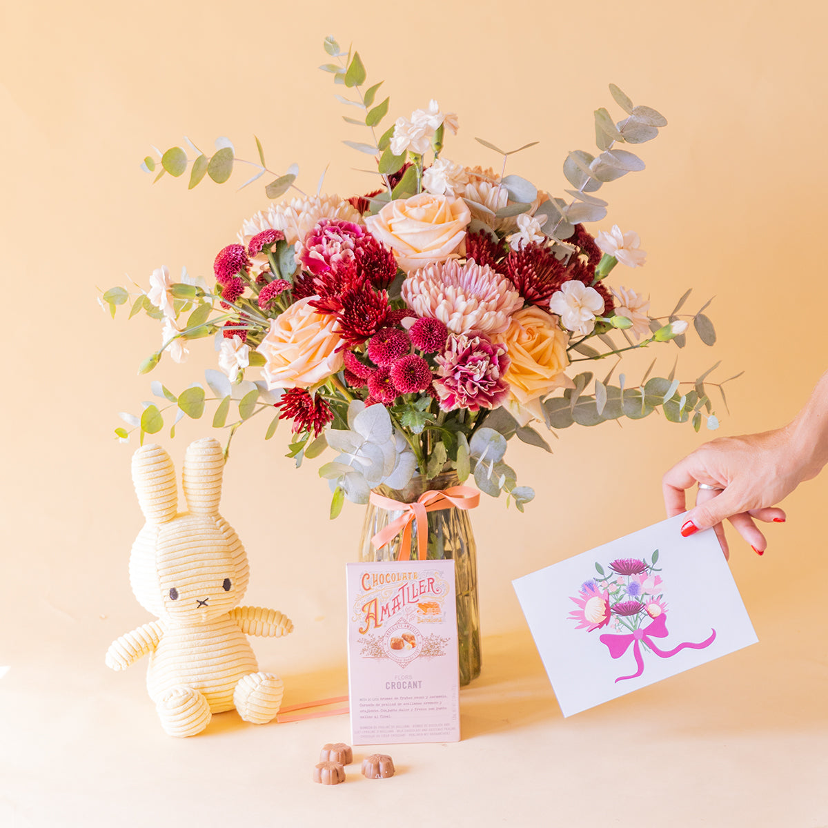 mano sosteniendo la tarjeta Protea junto al ramo Solsticio, Miffy y bombones