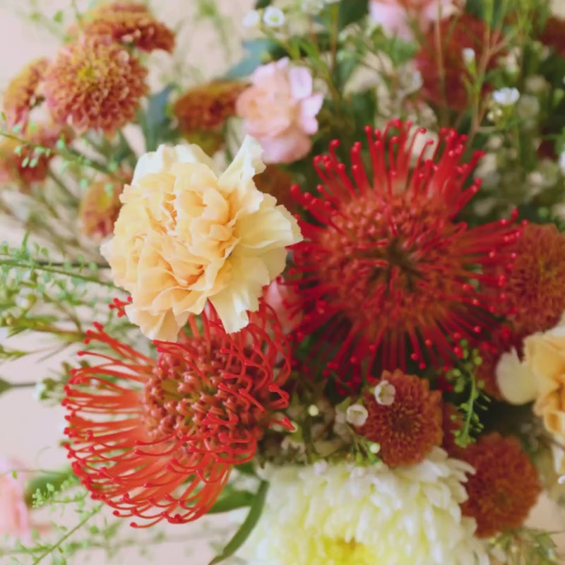 Vídeo de detalle del ramo de verano de Colvin La Jarana con proteas alfiletero de color naranja, crisantemos y flores crema.