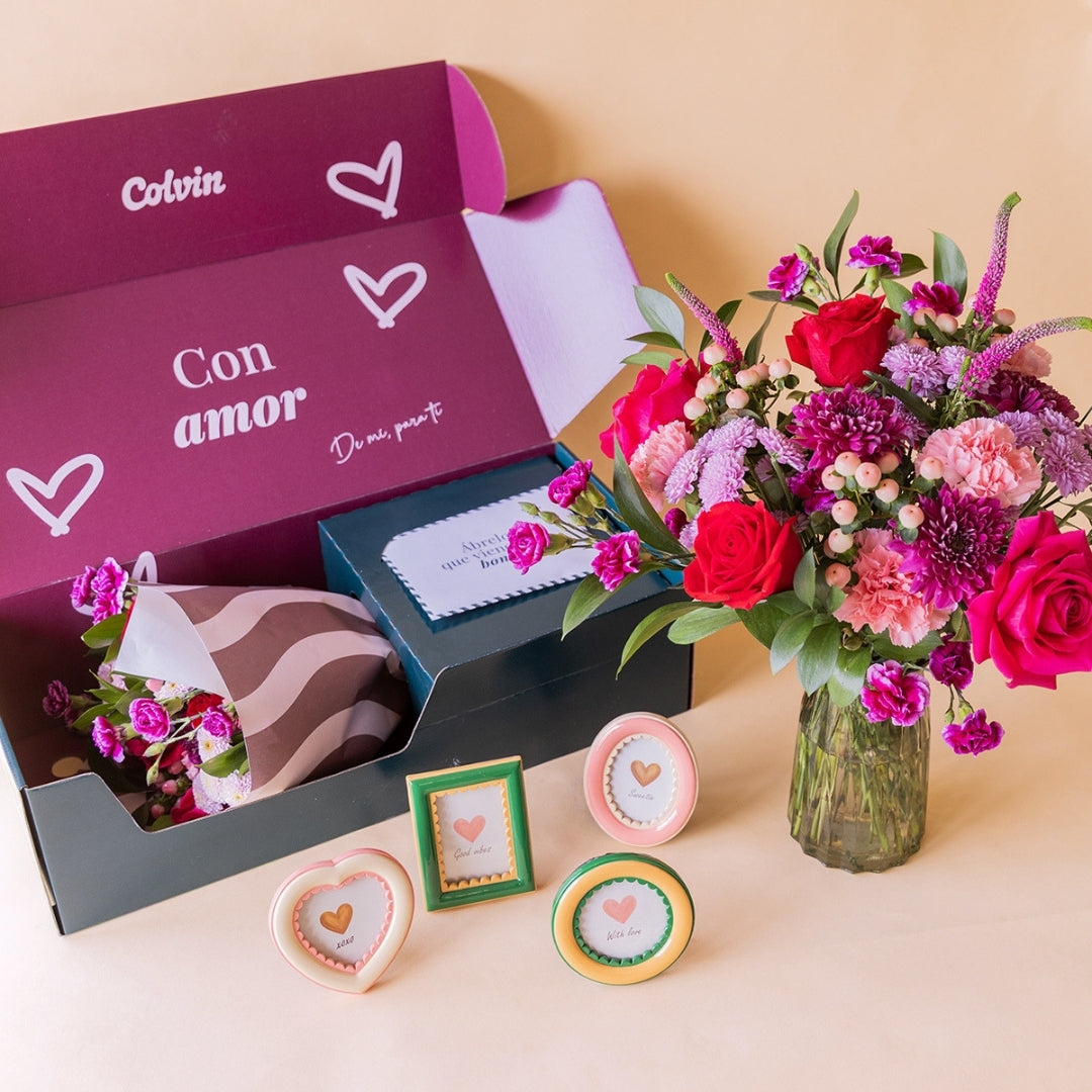 Kit "Para el Recuerdo" de Colvin: ramo de flores rojas en jarrón de cristal junto a caja "Con amor" abierta con cuatro marcos de fotos decorativos en formas de corazón, óvalo, rectángulo y círculo