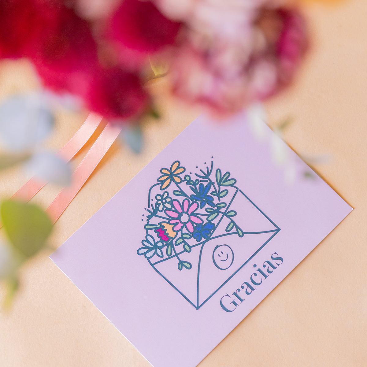 detalle macro de la tarjeta Gracias con ilustración de sobre floral, ramo desenfocado al fondo